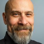 Close-up portrait of a mature bald man with a full beard, exuding confidence and style in a professional studio setting.